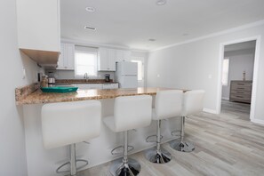 A modern kitchen with white cabinets, a granite countertop, and three white bar stools.