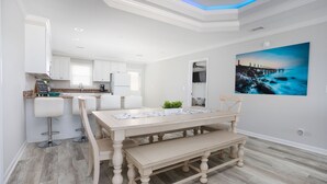 A modern kitchen with white cabinets, a dining area with a wooden table and benches, and a large painting on the wall. - Pool Paradise: 8 bedroom 6 bath private pool sleeps 20 across from the beach! (Murrells Inlet)