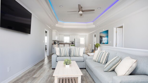 A modern living room with a grey sofa, a wooden coffee table, and a ceiling fan. - Pool Paradise: 8 bedroom 6 bath private pool sleeps 20 across from the beach! (Murrells Inlet)