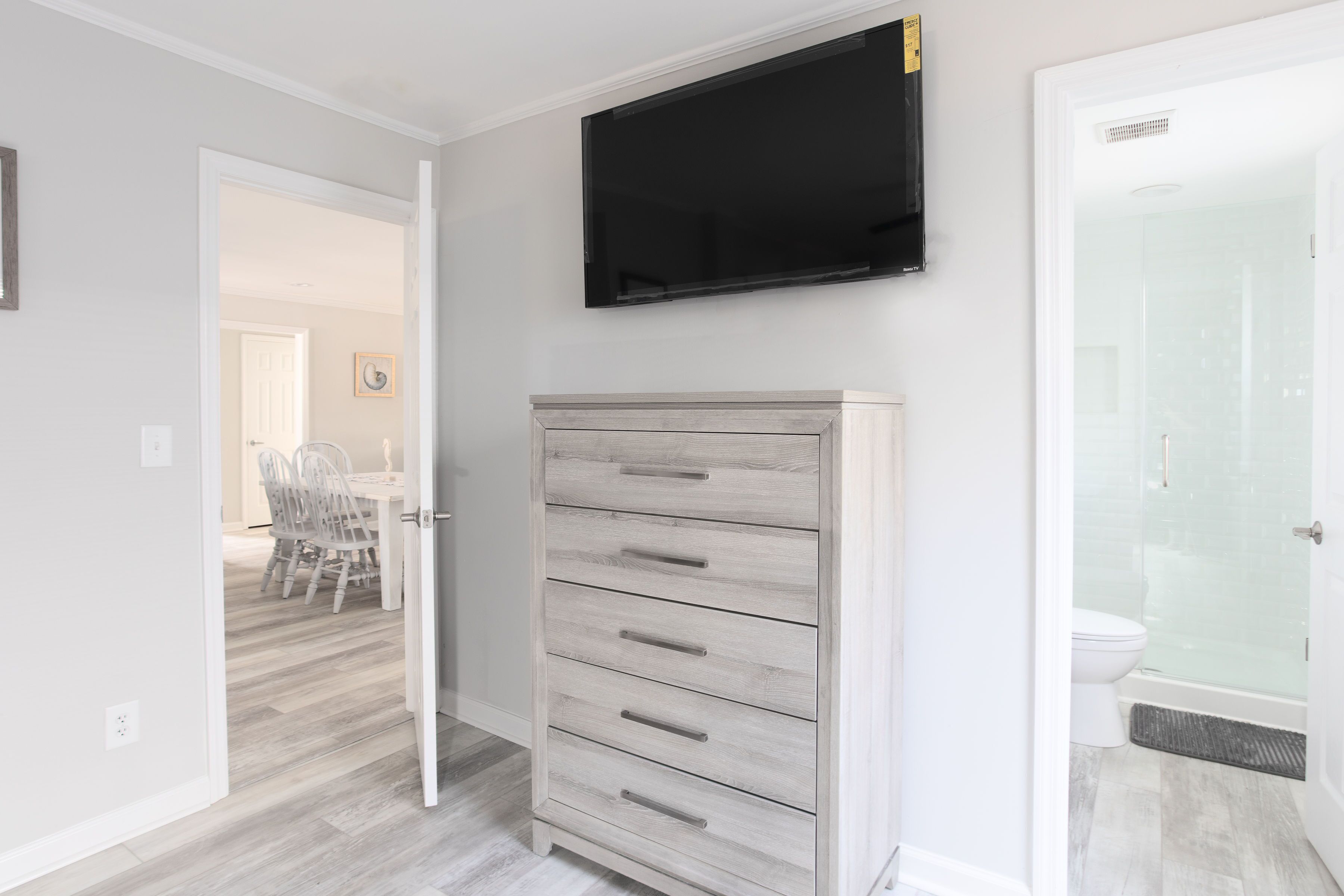 A room with a wooden dresser, a mounted TV, and a shower area.