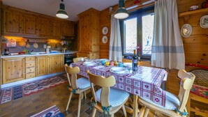 A wooden cabin kitchen with a dining table set for four, wooden cabinets, and a large window with curtains. - Casa Cisi ski in-Ski out 20m, Livigno, Italy (Livigno)