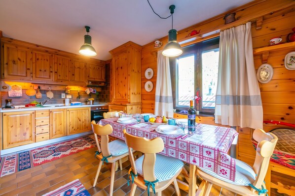 Ein Holzblockhaus-Innenraum mit einem Esstisch für vier Personen, Holzausstattung und einem Fenster mit Vorhängen.