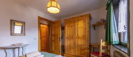 A room with a bed, wooden wardrobe, a small table, and a chair.