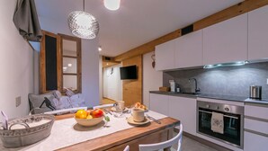 A modern kitchen with white cabinets, a wooden countertop, and a built-in oven. There is a dining table with a bowl of fruit and a cup. - Menina, Livigno, Italy (Livigno)