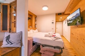 A hotel room with a bed, a television mounted on the wall, and a wooden ceiling.