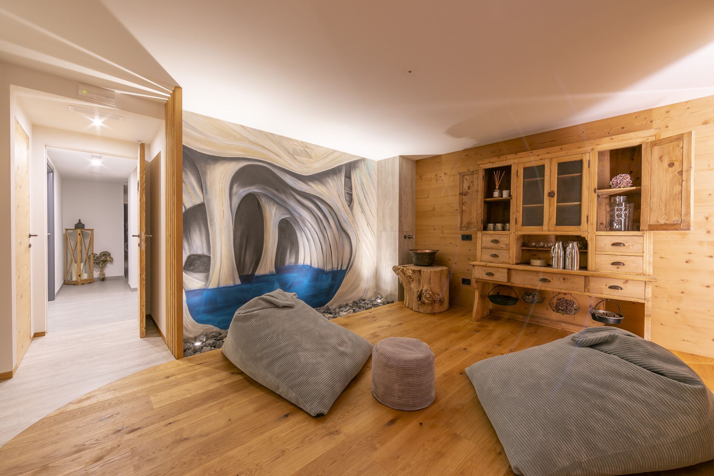 A room with wooden flooring, a large abstract mural on the wall, and a wooden cabinet with various items.