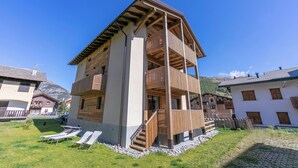 A multi-story building with a wooden balcony, a staircase, and a grassy area with sun loungers. - Giulia, Livigno, Italy (Livigno)
