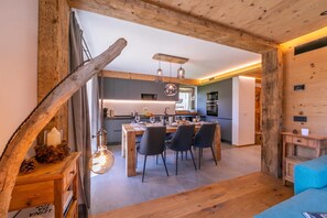 A modern kitchen with a dining area, wooden beams, and pendant lighting.