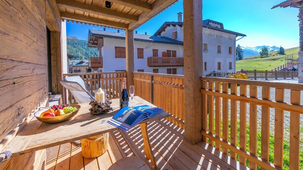 A wooden deck with a table, a bowl of fruit, a bottle, and a magazine. - Giulia, Livigno, Italy (Livigno)