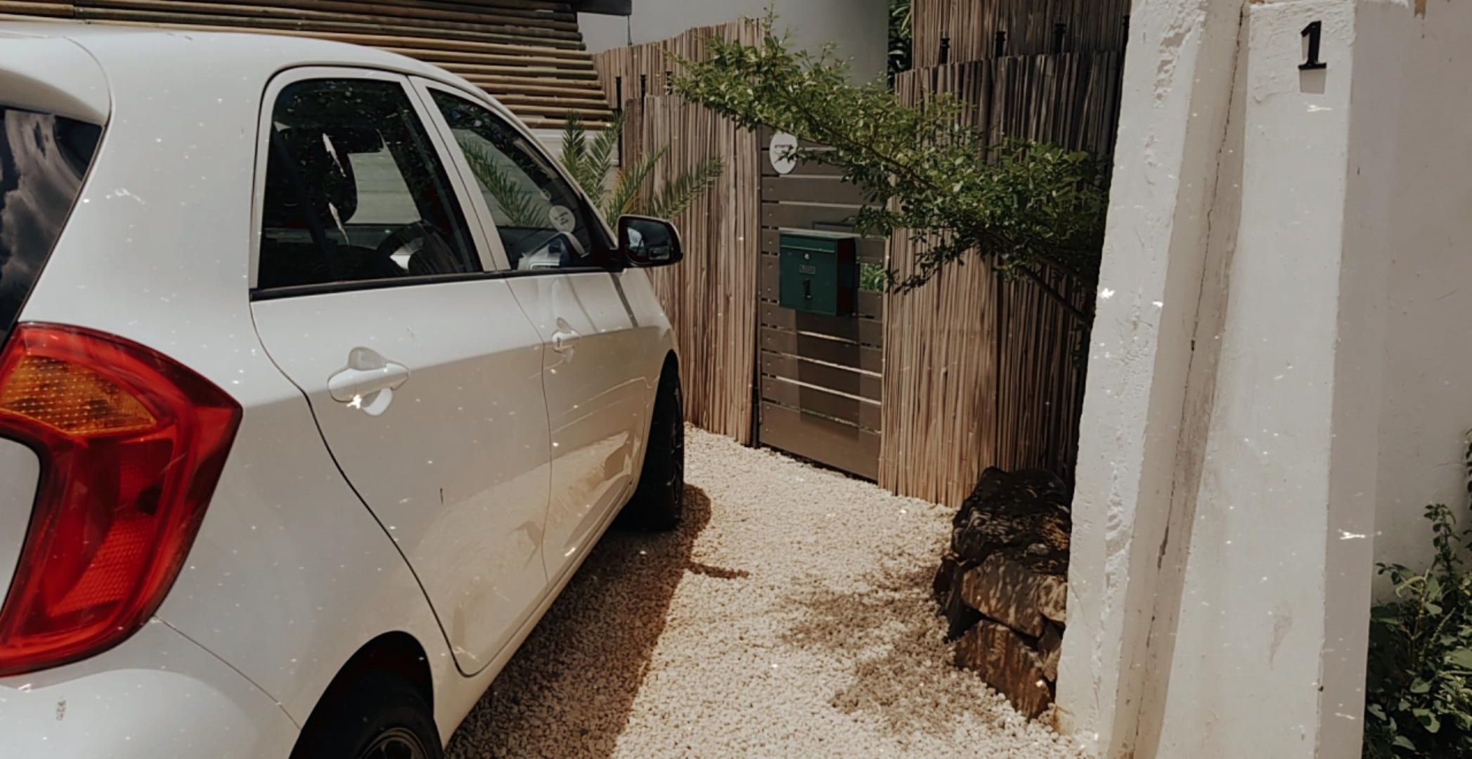 A white car parked in a driveway with a wooden fence and a gate.