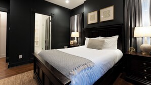 A bedroom with a large bed, dark walls, and a wooden headboard. There are two bedside tables with lamps and a nightstand with a lamp.