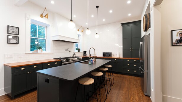 A modern kitchen with dark cabinetry, a central island with stools, pendant lighting, and a view of the outdoors through a window.
