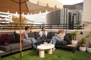 A rooftop seating area with a sofa and a table, surrounded by potted plants, under a large umbrella. - Little Drifter Canberra (Canberra)