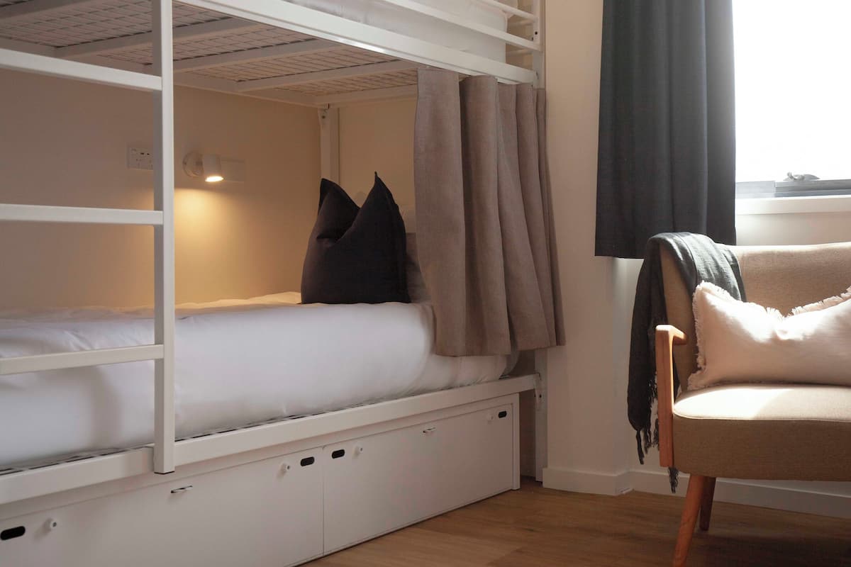 A bunk bed with storage drawers, a chair, and a window with curtains.