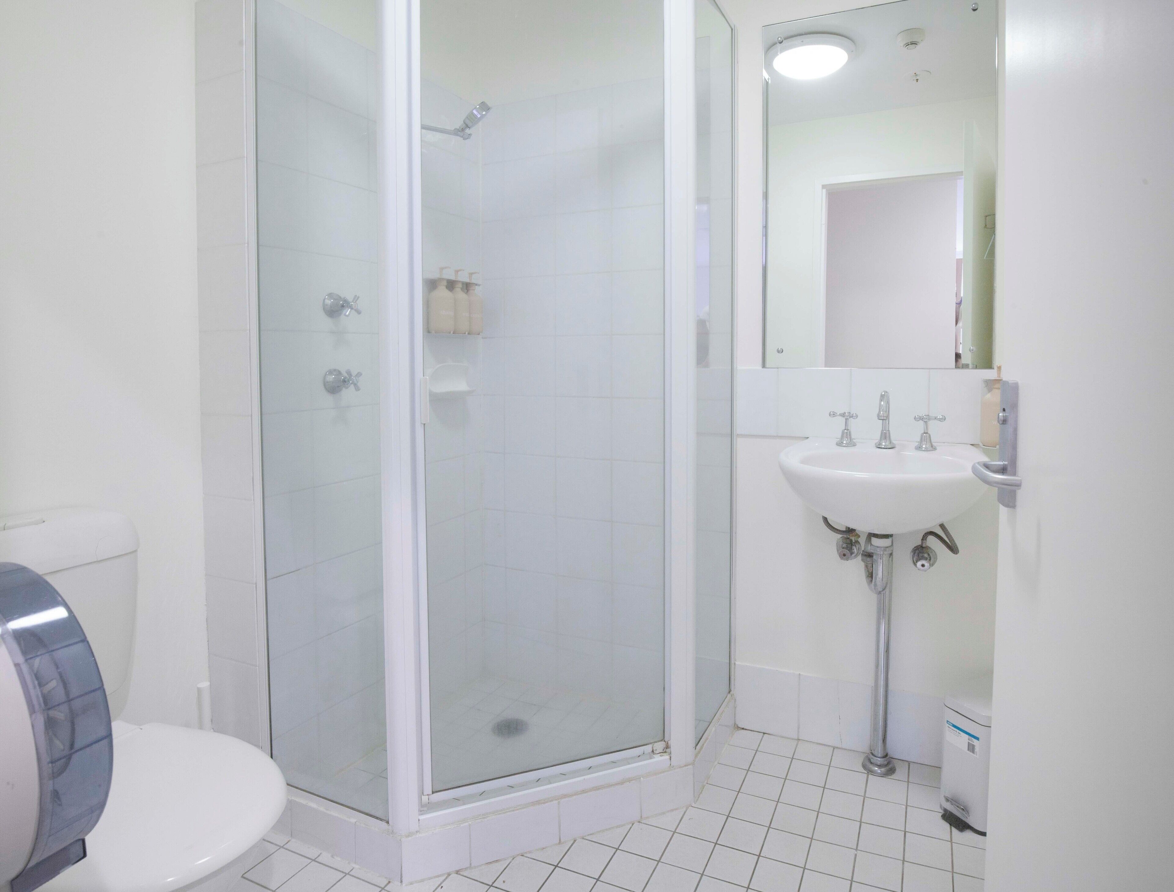 A bathroom with a toilet, a glass-enclosed shower, and a sink with a mirror.