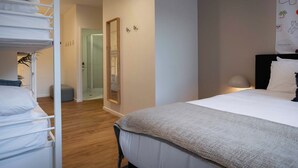 Habitación de hotel con cama, mesita de noche con lámpara, armario con ropa colgada y un espejo en la pared.