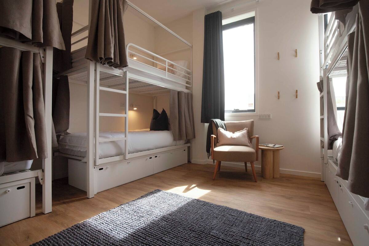 A bunk bed room with a desk and chair, a small rug, and curtains.