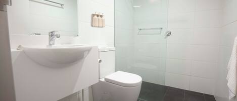 A modern bathroom with a white sink, toilet, and glass shower enclosure.