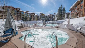 Ein Poolbereich mit Whirlpool, umgeben von Schnee, mit Gebäuden im Hintergrund.