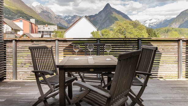 Una mesa de madera con sillas y una sombrilla en un balcón con vistas a la montaña.