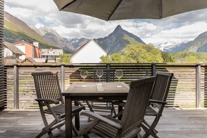 Una mesa de madera con sillas y una sombrilla en un balcón con vistas a la montaña.