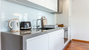 Una cocina moderna con encimera de granito, armarios blancos, pileta de acero inoxidable y horno empotrado.