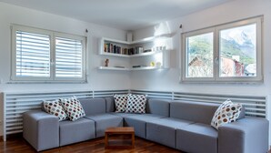 Una sala de estar moderna con un sofá seccional gris, una mesa de centro de madera, estanterías empotradas y ventanas grandes con persianas.
