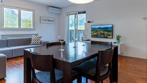 Un comedor moderno con una mesa y sillas de madera, un sofá con un cojín estampado y un ventanal con vistas a la montaña.