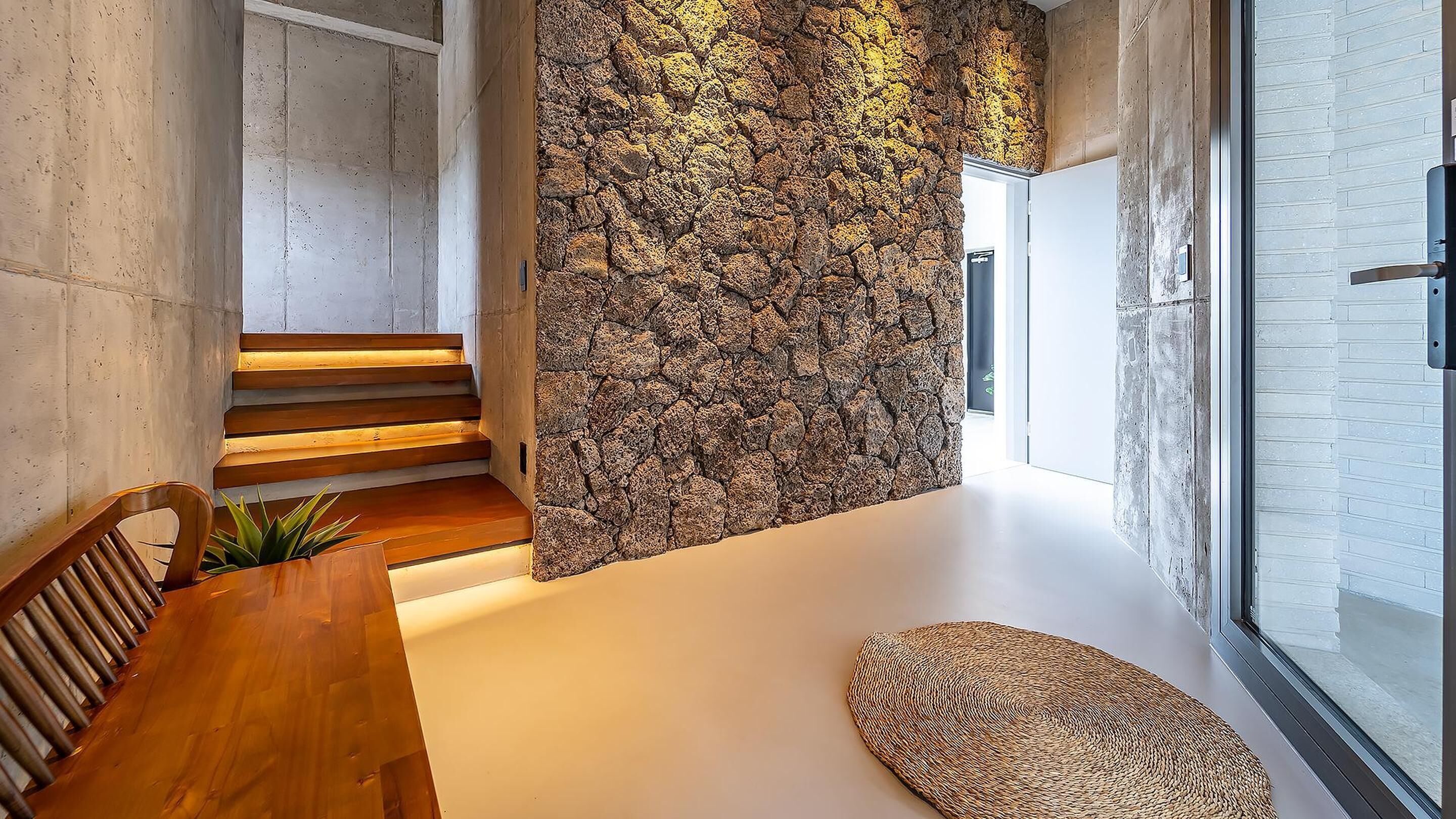 A modern interior with a stone wall, wooden staircase, and a dining area with a round rug.