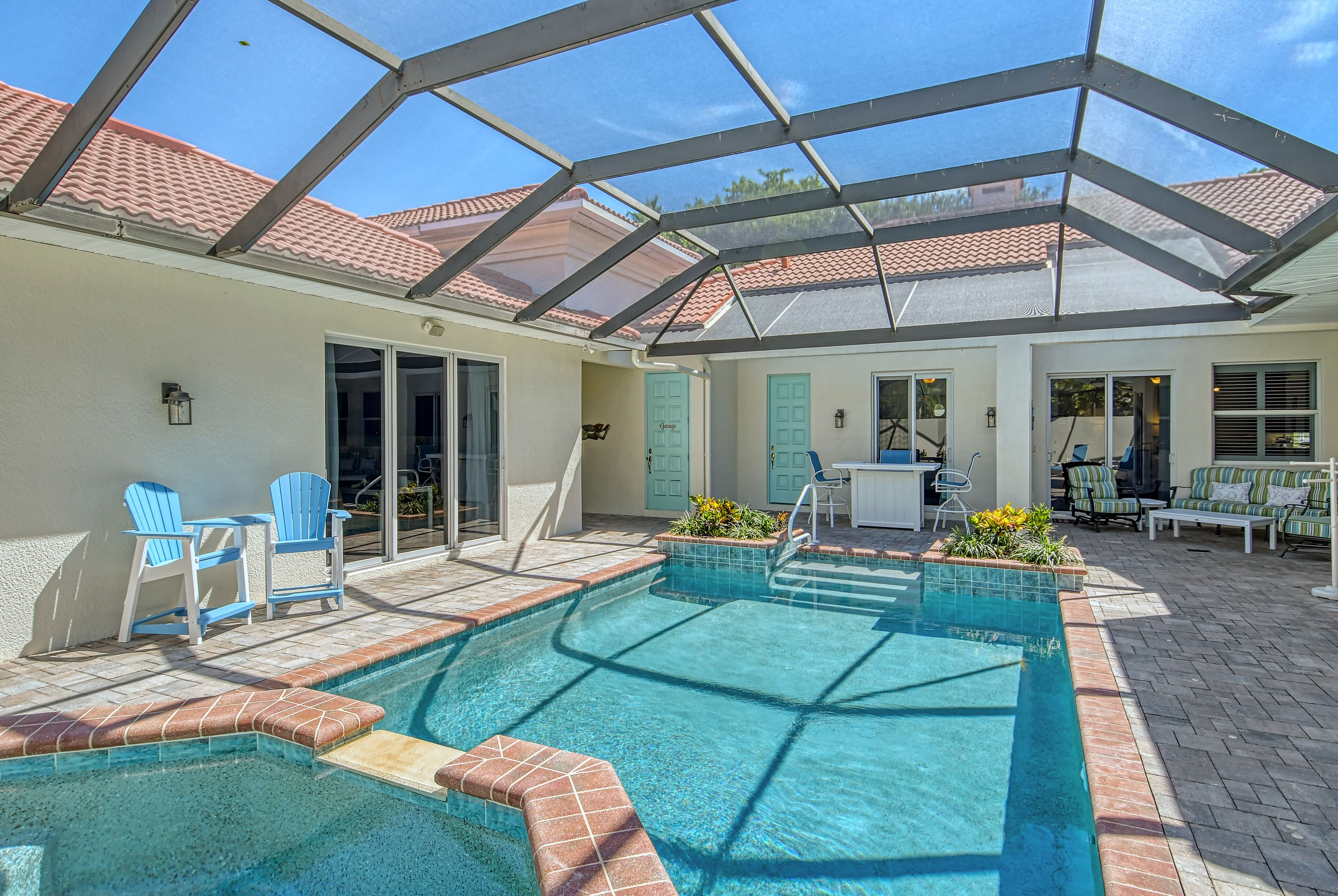 Une piscine dotée d’un toit en verre, de chaises bleues et d’un espace patio aménagé avec du mobilier d’extérieur.