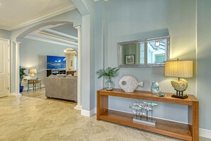 A spacious living area with a wooden console table, a television, and a decorative mirror. - Sunburst Courtyard | Pet Friendly Waterfront Home w/ Pool, Walk to Siesta Key Beach & Village! (Siesta Key)