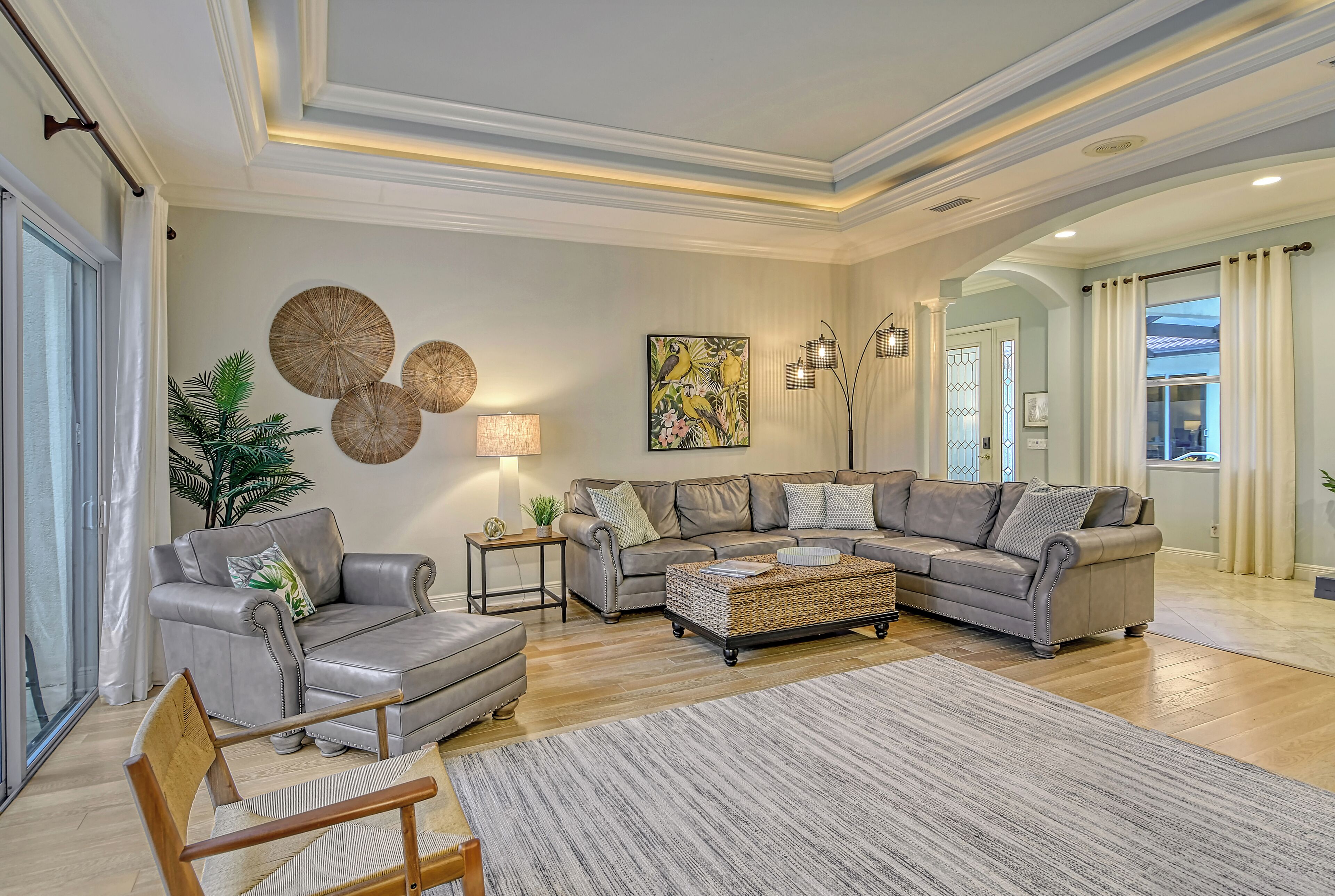 A spacious living room with a grey sectional sofa, a wooden chair, a woven coffee table, and a large rug.