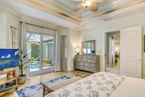 Un dormitorio amplio con una cama grande, un aparador, un televisor y vistas a una piscina a través de puertas corredizas de vidrio.