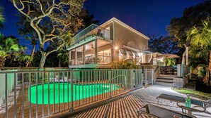 Una casa de dos pisos con piscina, mobiliario exterior y un patio cubierto.