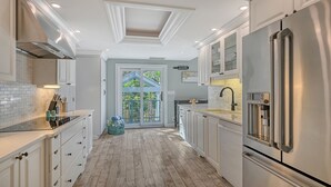 Una cocina moderna con muebles blancos, un refrigerador de acero inoxidable y piso de madera.