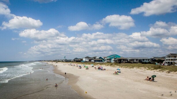 A beach with houses in the background and people on the sand. - Dog Friendly Cottage w/ Large Fenced in Backyard - Close to Beach (Oak Island)