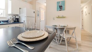 A modern kitchen with white cabinets, a coffee machine, and a dining area with a table set for two. - Dog Friendly Cottage w/ Large Fenced in Backyard - Close to Beach (Oak Island)
