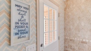 A door with a window, a wall with a patterned wallpaper, and a framed sign with text. - Dog Friendly Cottage w/ Large Fenced in Backyard - Close to Beach (Oak Island)
