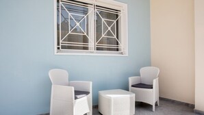 A room with two white wicker chairs and a matching ottoman, a window with white shutters, and a light blue wall.