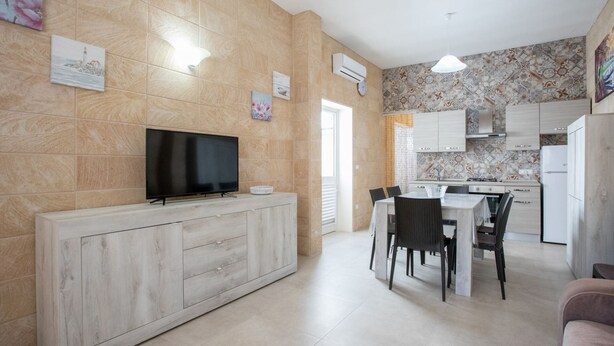 A modern kitchen with a flat-screen TV, dining table, chairs, and a refrigerator.