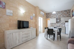 A modern kitchen with a flat-screen TV, dining table, chairs, and a refrigerator. - Bea Apartment | 2-bedroom house, Wi-Fi, air conditioning (Porto Cesareo)