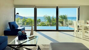Un salon moderne doté d’une grande porte vitrée donnant accès à une piscine et offrant une vue sur l’océan.