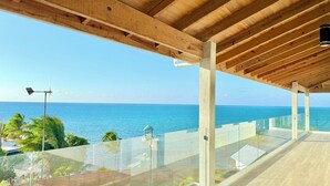 Un balcon extérieur moderne offrant une vue dégagée sur l’océan, avec des poutres en bois au plafond et une balustrade en verre.