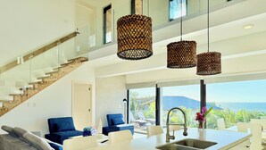 Une cuisine moderne dotée d’un îlot central, d’un coin repas avec des chaises, d’un canapé et d’un escalier avec des rampes en verre.