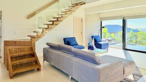 Un salon moderne avec un escalier en bois, un canapé gris et deux fauteuils bleus.