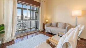 A hotel room with a balcony, a sofa, a chair, a lamp, and a view of the outside. - Central Apartment Near the Beaches (Lagos)