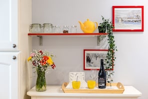 A kitchen counter with a vase of flowers, a yellow teapot, and a wine bottle on a tray.