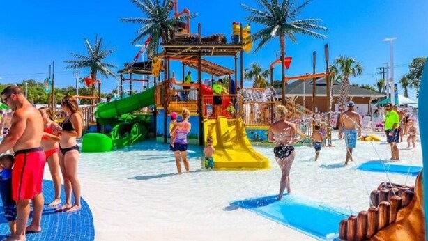 Un parque acuático con toboganes y estructuras de juego, rodeado de palmeras.