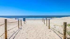 Una playa arenosa con una cerca de madera que conduce al agua.
