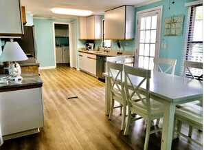A kitchen with white cabinets, a dining table with chairs, a lamp, and a sign on the wall.